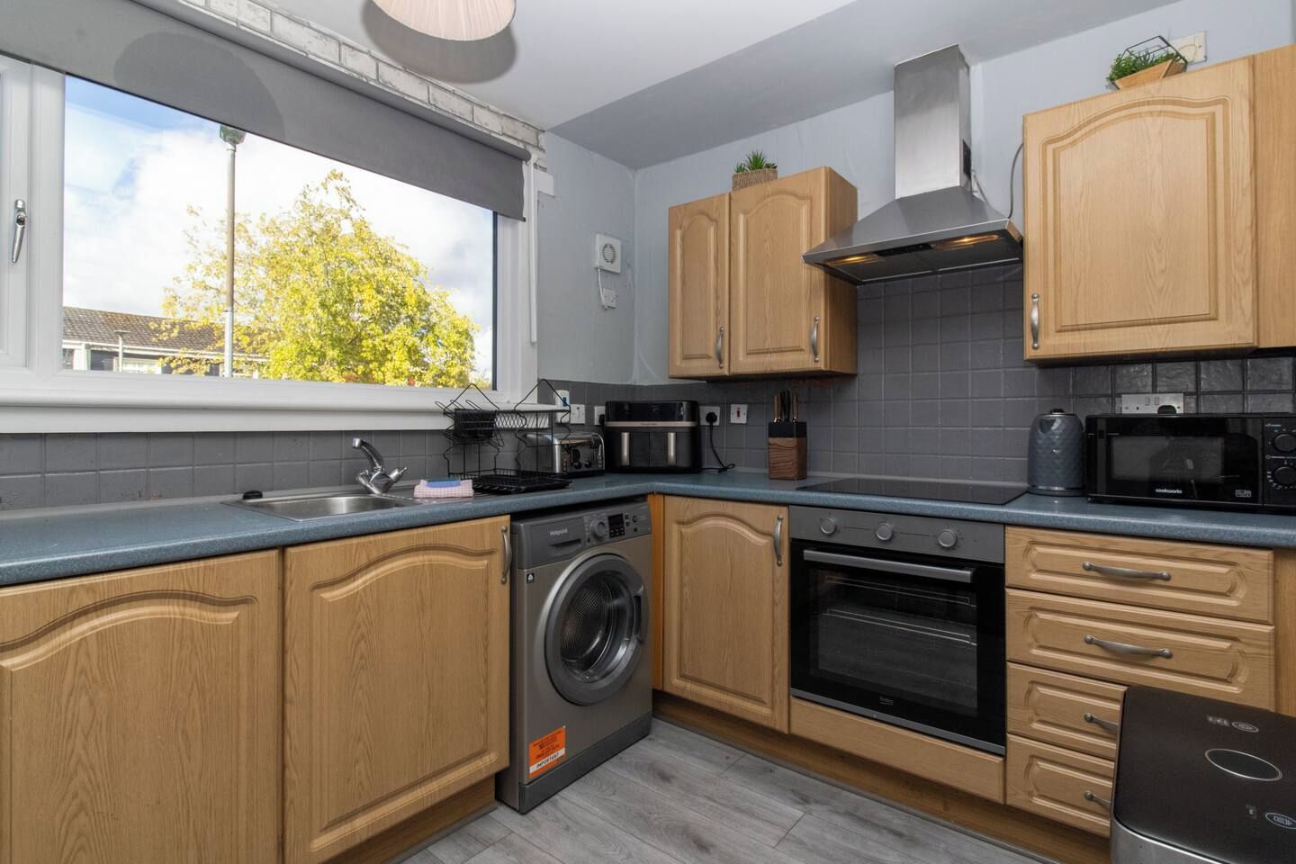Une cuisine moderne avec des meubles en bois, un lave-linge, un four et un four à micro-ondes.