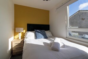 A hotel room with a bed, a nightstand, a lamp, and a window. - East Kilbride 3BR Retreat | Free Parking |Sleeps 6 (East Kilbride)