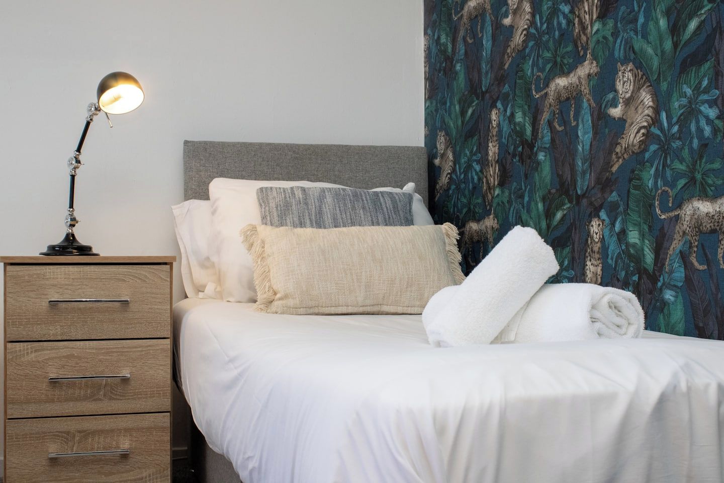 Un letto rifatto con lenzuola bianche, una testiera grigia e una parete decorata alle spalle.