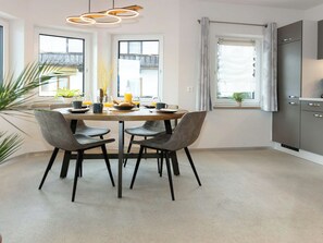 A modern kitchen with a dining area, featuring a round table with chairs, a hanging light fixture, and a view through the windows. - Nice apartment for 15 people with WIFI, TV, terrace and pets allowed (Wildschönau)