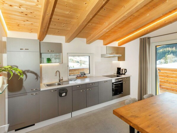 Una cocina moderna con armarios grises, un lavamanos de acero inoxidable y una mesa de comedor de madera.