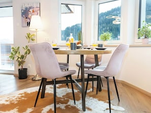 Ein Essbereich mit einem runden Tisch, vier Stühlen, einem Kuhfellteppich und Blick auf Berge durch große Fenster.