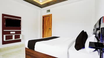 A hotel room with a bed, a TV mounted on the wall, a wooden door, and a ceiling with recessed lighting.