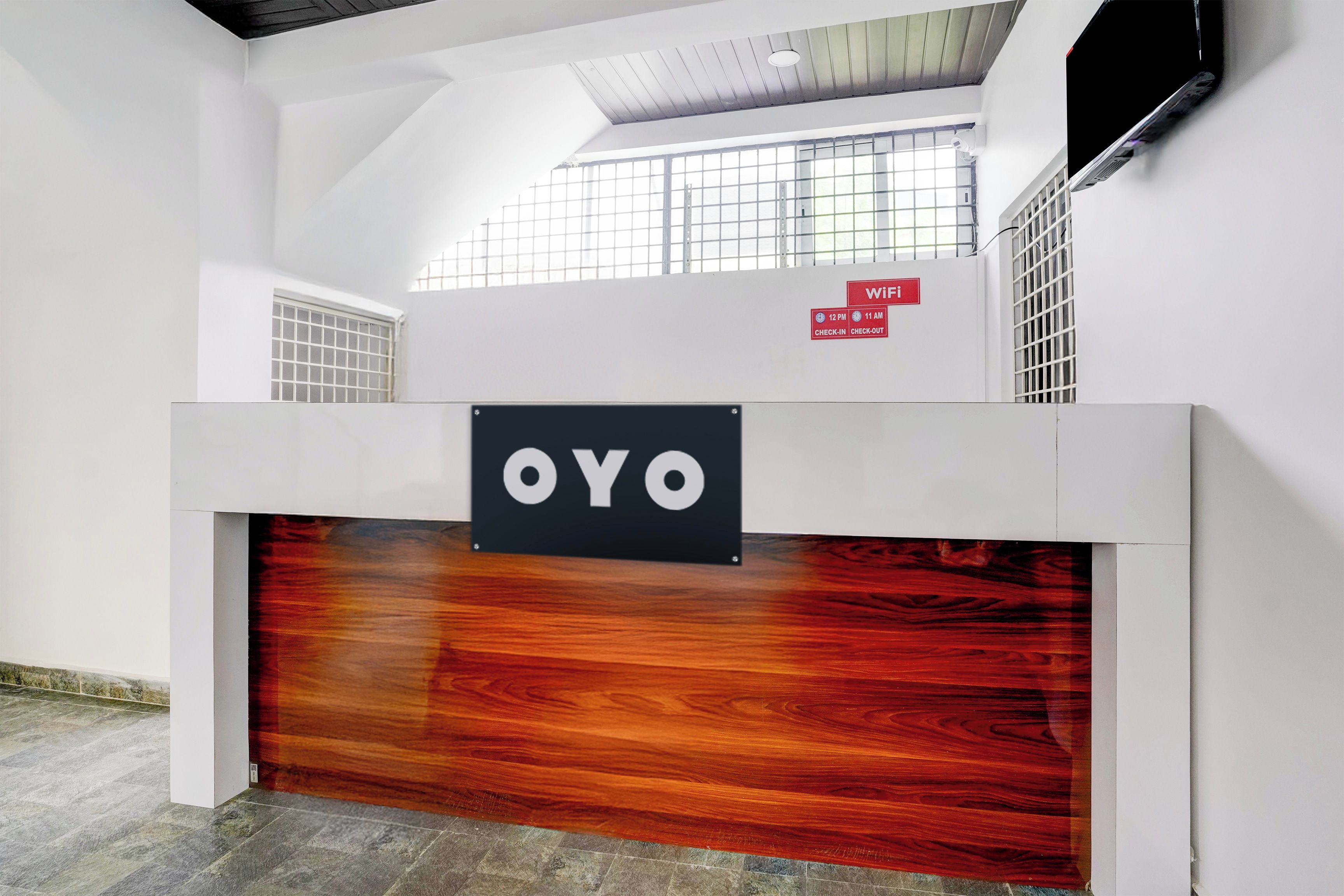 A reception desk with a sign that reads 'OYO' and a WiFi sign indicating check-in at 12 PM and check-out at 11 AM.