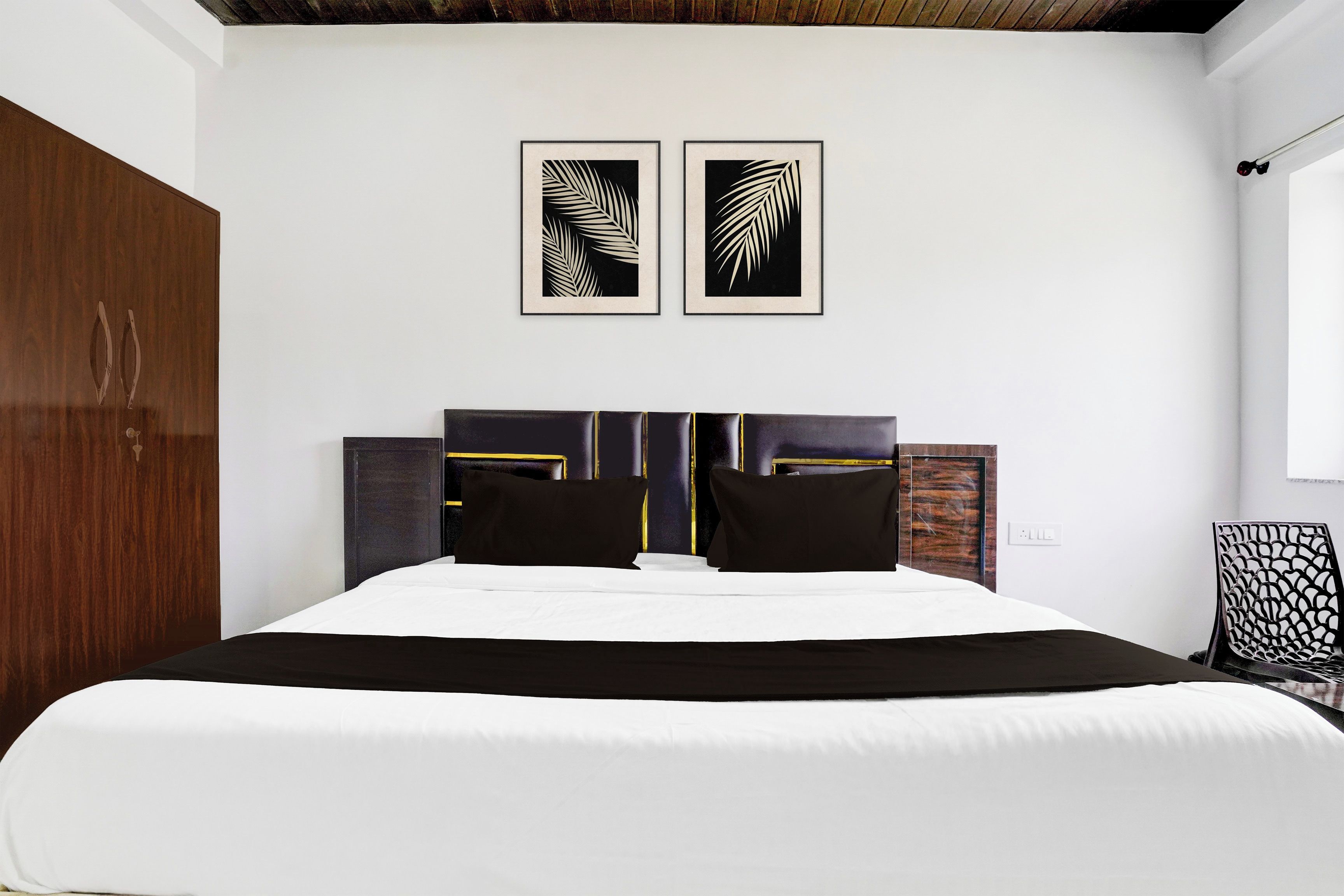 Un dormitorio con una cama, dos cuadros con hojas, un armario y una silla.