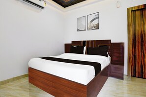 A bedroom with a wooden bed, white bedding, a wooden headboard, and two wall-mounted artworks. - HOTEL O ROYAL INN (Nagpur)