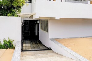 A white building with a covered entrance and a small outdoor area with a sandy surface. - HOTEL O ROYAL INN (Nagpur)