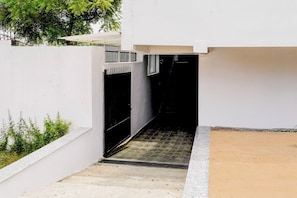 Un estrecho sendero de concreto que conduce a una verja negra, rodeada por muros blancos y un pequeño jardín.