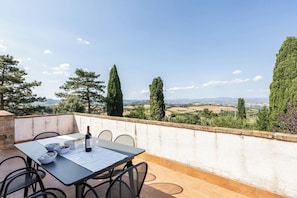 Un patio al aire libre con una mesa lista para dos personas, una botella de vino y cuencos con comida.
