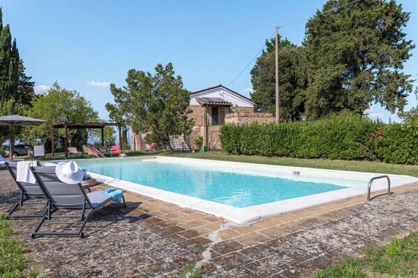 Una piscina con sillas de descanso, un edificio de piedra y cielo despejado.