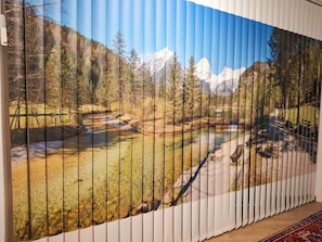 Ein Zimmer mit großem Panoramablick auf eine gebirgige Landschaft durch vertikale Jalousien.