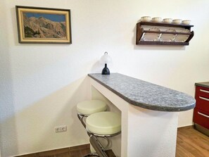 A kitchen with a granite countertop, two bar stools, a hanging light, a framed picture, and a shelf with bowls. - Cosy apartment for 4 people with WIFI, TV, patio, pets allowed and panoramic view (Weißenbach)