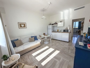 A modern living room with a sofa, a dining table, and a kitchen area. - Beautiful apartment for 4 people with A/C, WIFI, TV and patio (Mola Di Bari)
