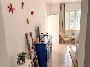 Eine moderne Küche mit einer blauen Kochinsel, Holzstühlen, einem kleinen Tisch mit einer Pflanze und Blick ins Freie durch ein Fenster.