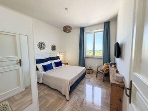 A bedroom with a bed, bedside tables, a TV, a window with curtains, and a view of the outdoors. - Beautiful apartment for 4 people with A/C, WIFI, TV and patio (Mola Di Bari)