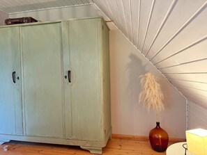 Una habitació amb un armari verd, un vas amb flors de plàntana seques, i una làmpada encèsa a terra.
