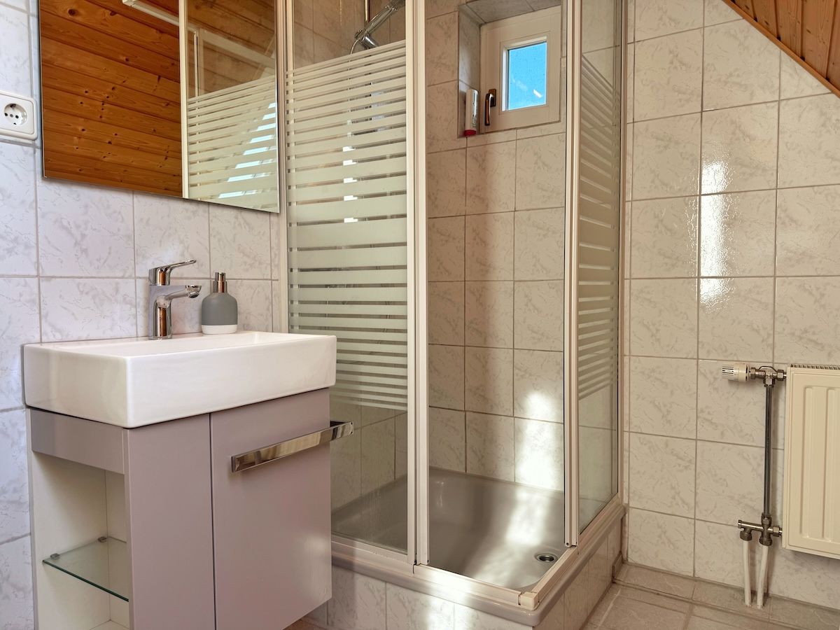 Ein Badezimmer mit Duschkabine aus Glas, einem Waschbecken mit Spiegel darüber und einem Handtuchhalter.