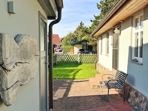 A patio area with a bench, a stone wall, and a view of a green lawn and a building in the background. - Vrbo Property (Polchow)