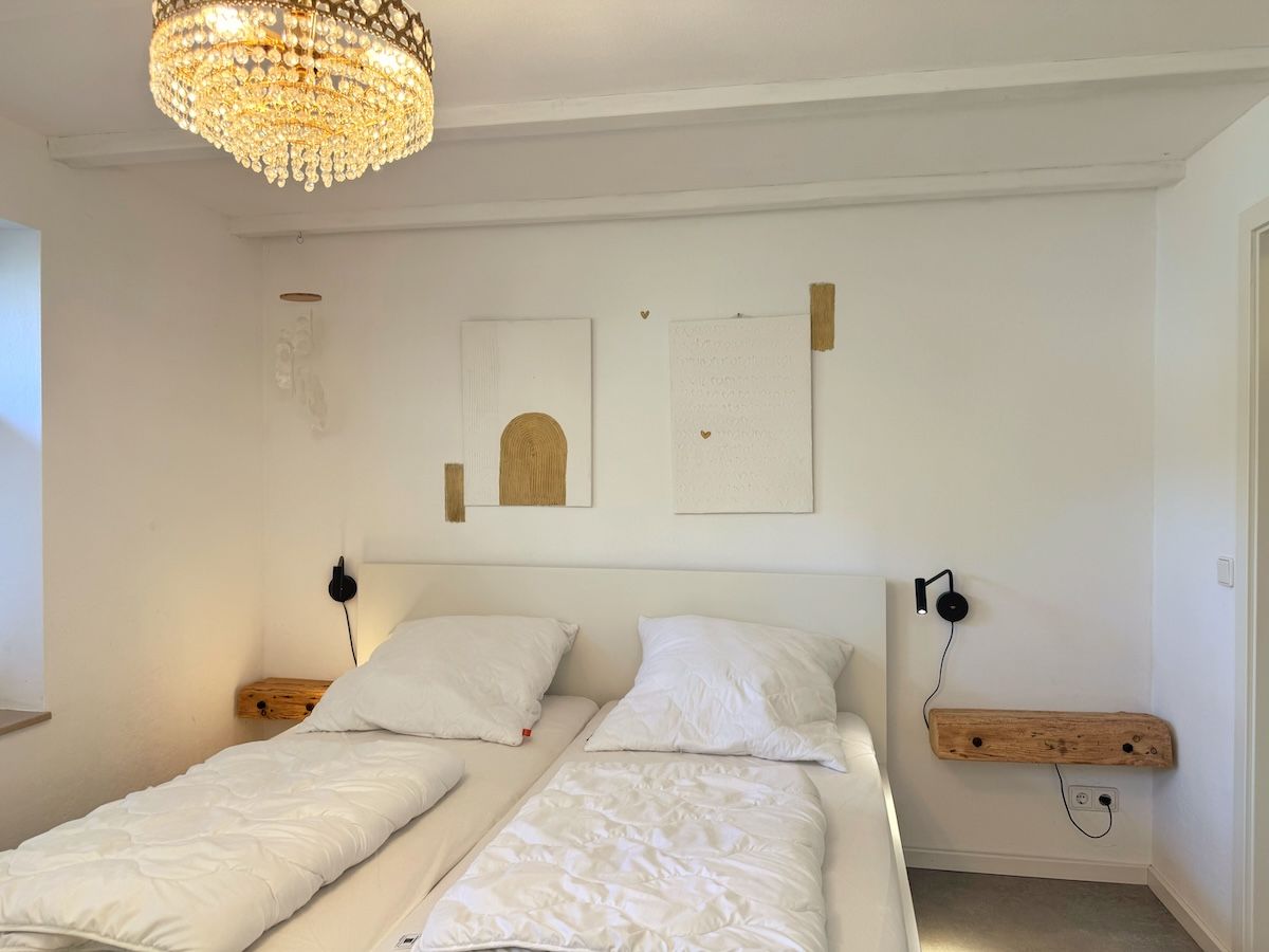 A bedroom with two beds, a chandelier, wall-mounted artwork, and a shelf with headphones.