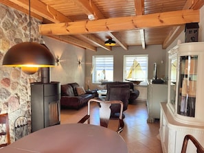 A cozy living room with a stone wall, a fireplace, a dining area, and a large window with a view. - Vrbo Property (Polchow)