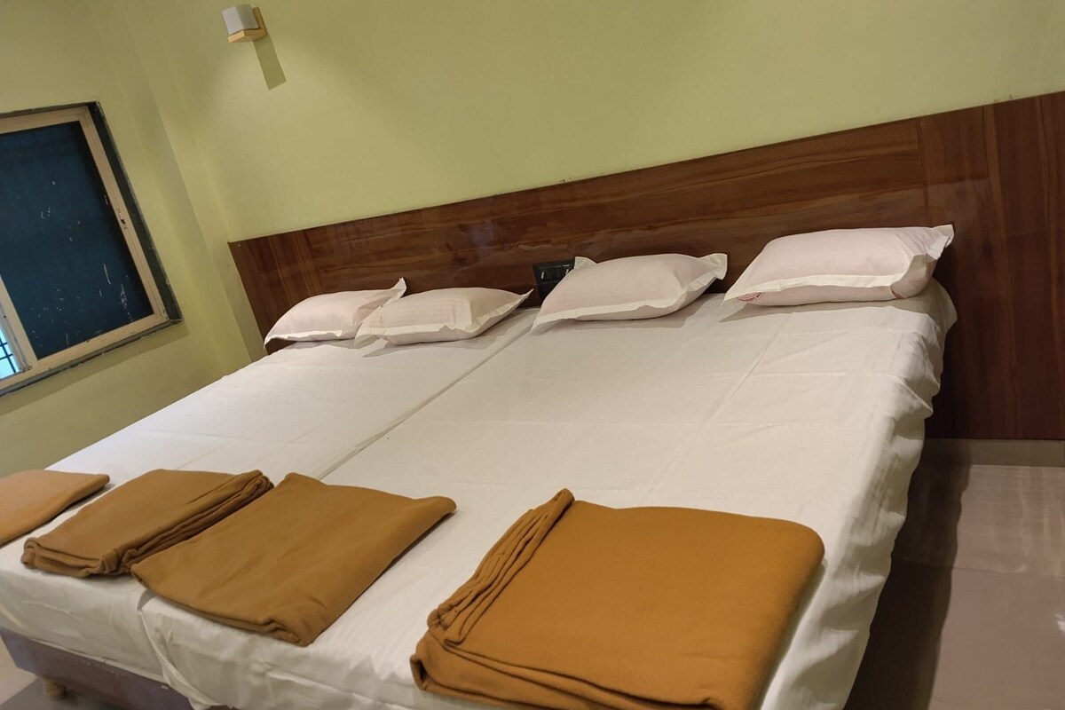 Cama doble con sábanas blancas y cuatro almohadas, cabecero de madera y lámpara fijada a la pared.
