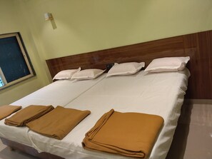Cama doble con sábanas blancas y cuatro almohadas, cabecero de madera y lámpara fijada a la pared.