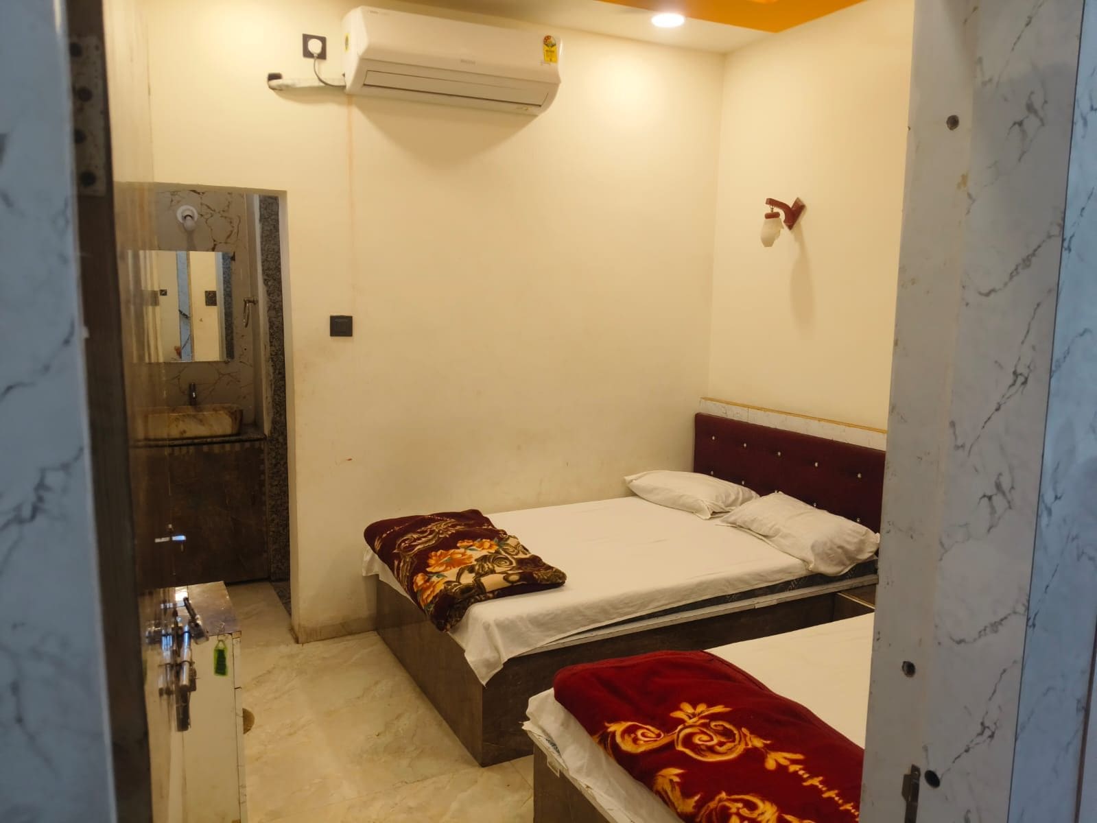 Una camera piccola con un letto singolo, pavimento in marmo, aria condizionata a muro, comodino e uno specchio.