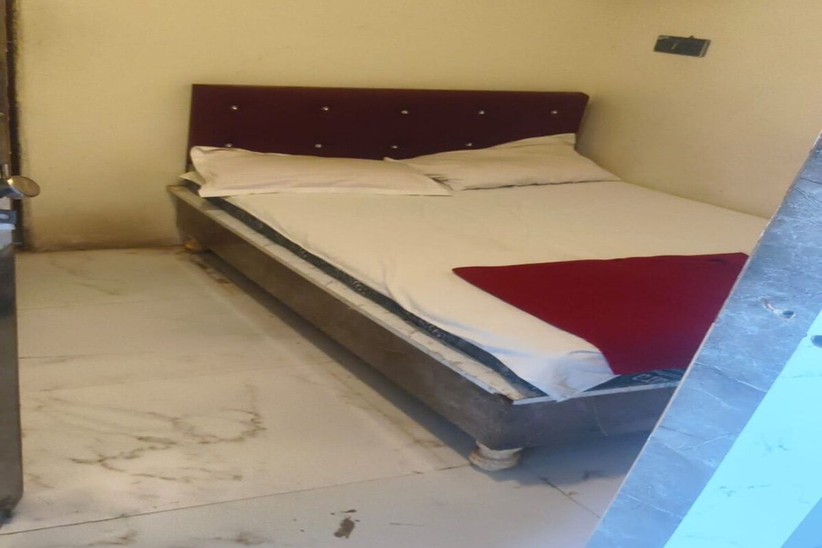 Una habitación pequeña con una cama individual, cabecera de madera y colchón blanco.