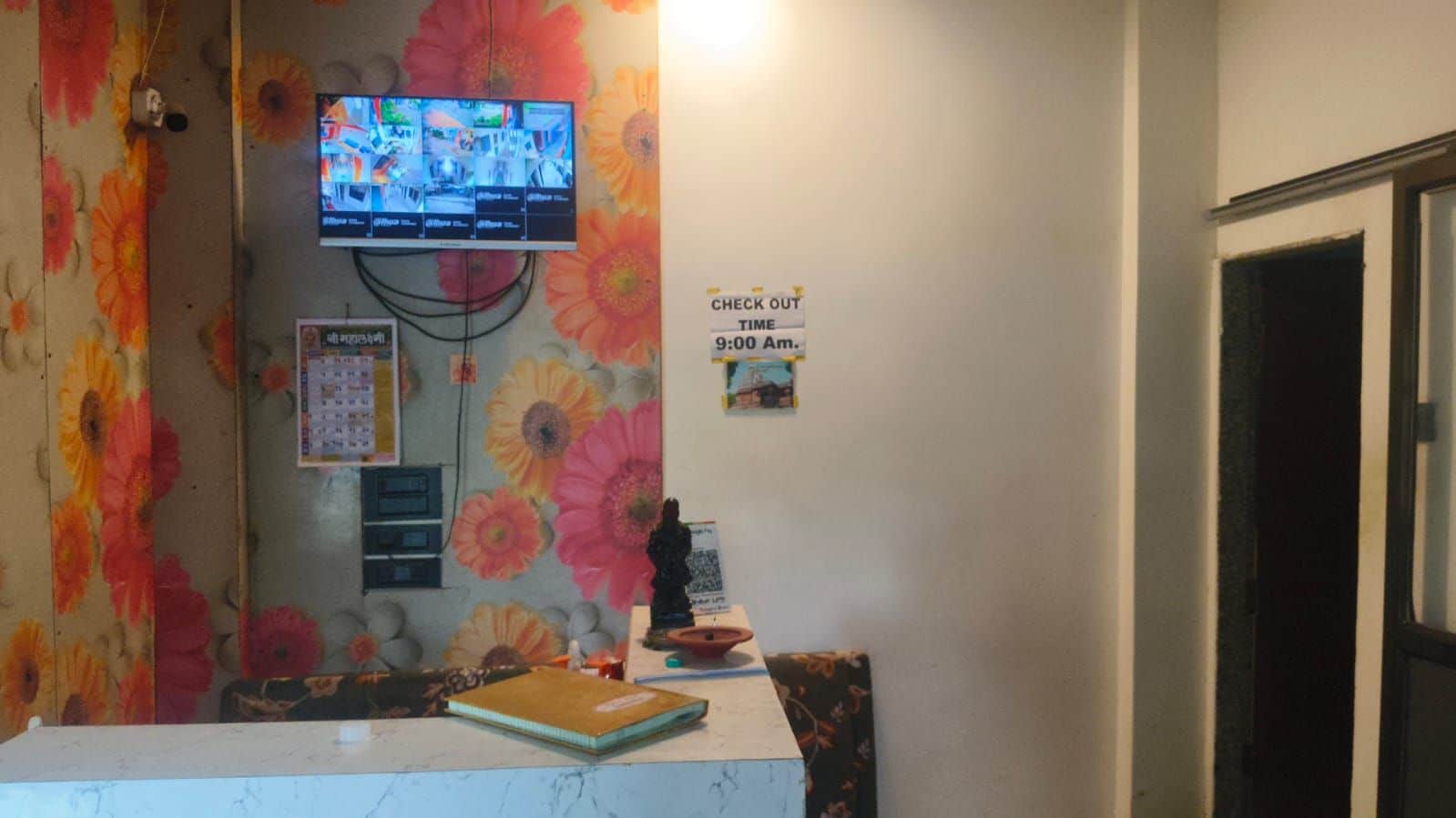 A reception area with a check-out time sign, a television mounted on the wall, and a floral-patterned curtain.