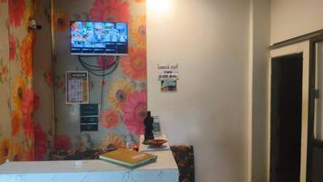 A reception area with a check-out time sign, a television mounted on the wall, and a floral-patterned curtain.