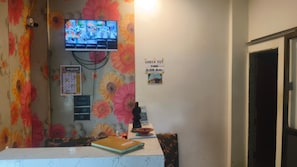 Un área de recepción con un cartel de horario de salida, un televisor montado en la pared y una cortina con estampado floral.