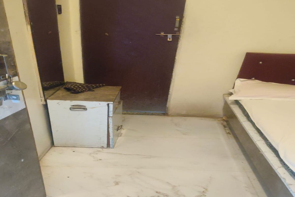 Un pasillo estrecho con piso de baldosas blancas, un mueble pequeño blanco y una cama con cabecera de madera.