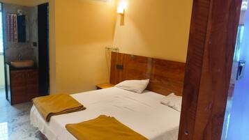 A hotel room with a bed, a wooden headboard, a nightstand, a wall-mounted air conditioner, and a bathroom with a sink and mirror.