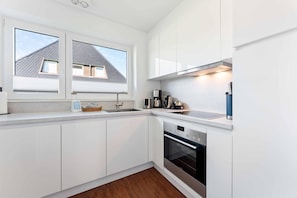 Una cuina moderna amb armaris blancs, forn integrat i finestra amb vista a una casa.