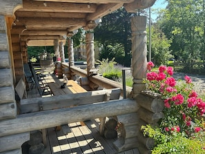 Une terrasse en bois agrémentée d’une pergola, d’un espace salon extérieur et d’un jardin où fleurissent des fleurs roses.