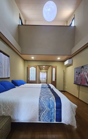 A hotel room with a large bed, a ceiling light, a door leading to another room, and a wall-mounted air conditioning unit. - Hanazonocho (Osaka)