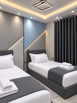 A modern hotel room with two beds, a grey headboard, and a large window with dark curtains. - Luxury Family 3BR Apartment - Steps to Pyramids, Grand Egyptian Museum & Saqqara (Giza Governorate)