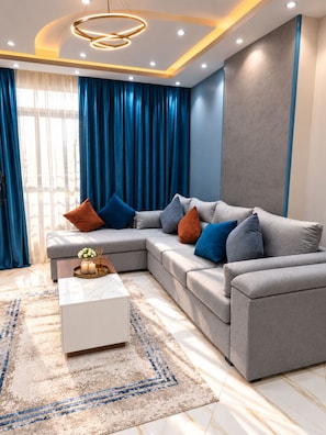 A modern living room with a sectional sofa, a coffee table, and a decorative rug. - Luxury Family 3BR Apartment - Steps to Pyramids, Grand Egyptian Museum & Saqqara (Giza Governorate)