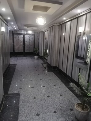 A hallway with a polished floor, potted plants, and a mirrored wall. - Luxury Family 3BR Apartment - Steps to Pyramids, Grand Egyptian Museum & Saqqara (Giza Governorate)