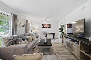 A living room with a sofa, coffee table, TV, and artwork on the walls. - Hot Tub Home Nr Airport | Yard Swing Set BBQ Games (San Antonio)