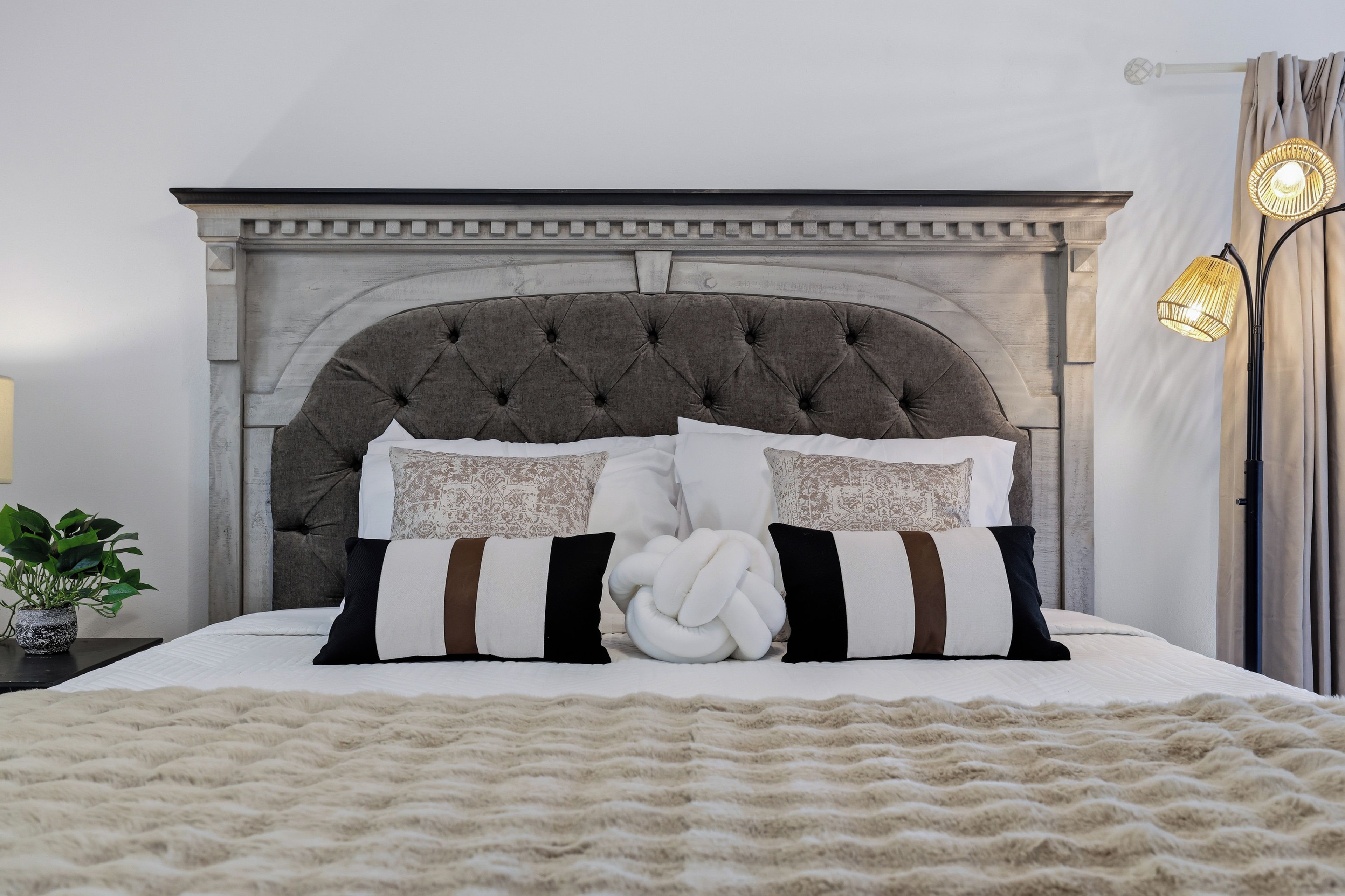 Ein Bett mit einer gepolsterten Kopfteil, zwei Zierkissen, einer weißen Tagesdecke und einer flauschigen Decke.