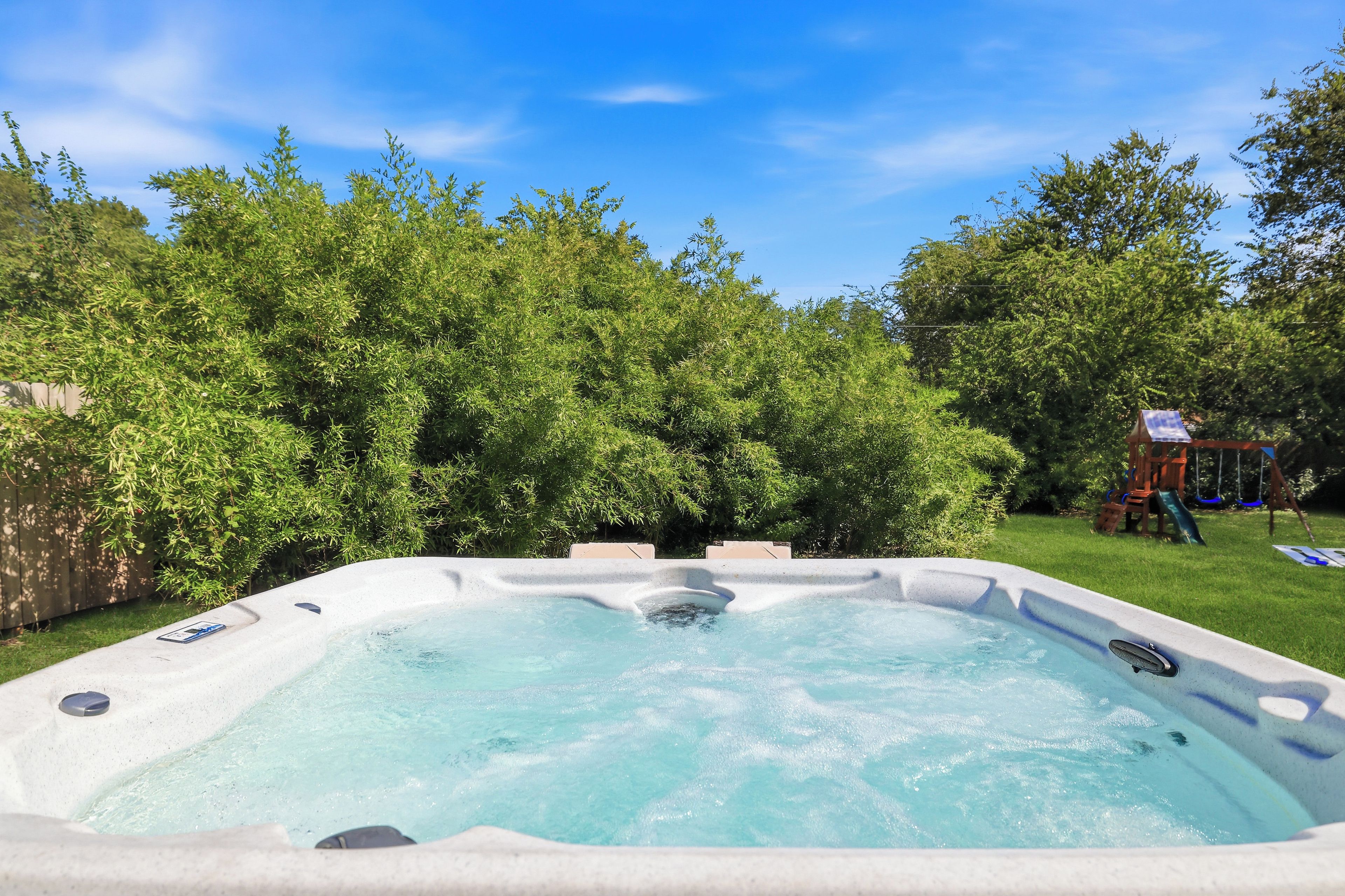 Un jacuzzi dans un jardin, entouré d’une végétation luxuriante et agrémenté d’une balançoire.