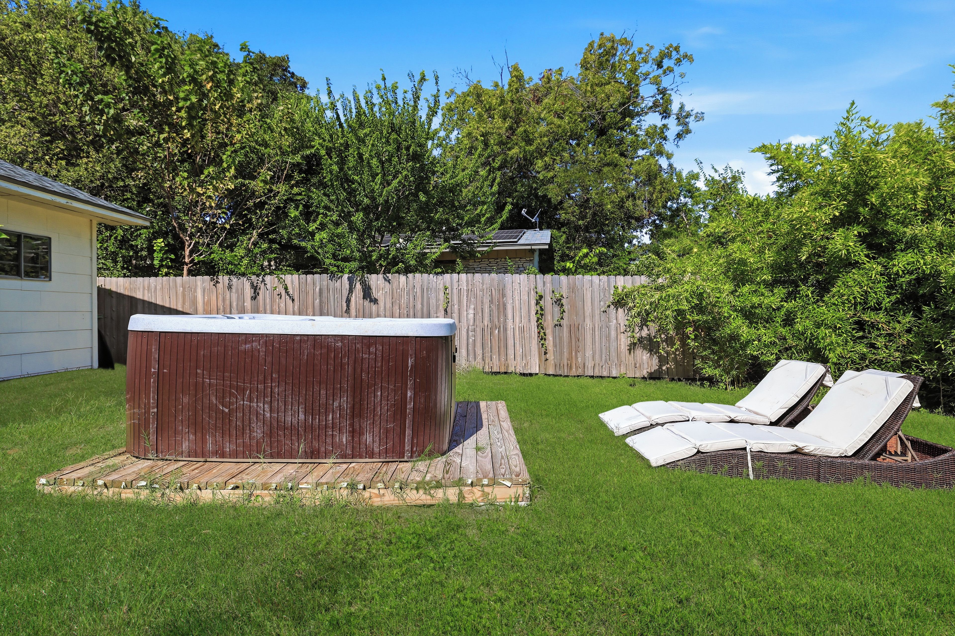 Un jardin avec un jacuzzi, des chaises longues et une clôture en bois.