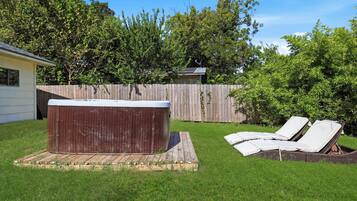 Un jardin avec un jacuzzi, des chaises longues et une clôture en bois.