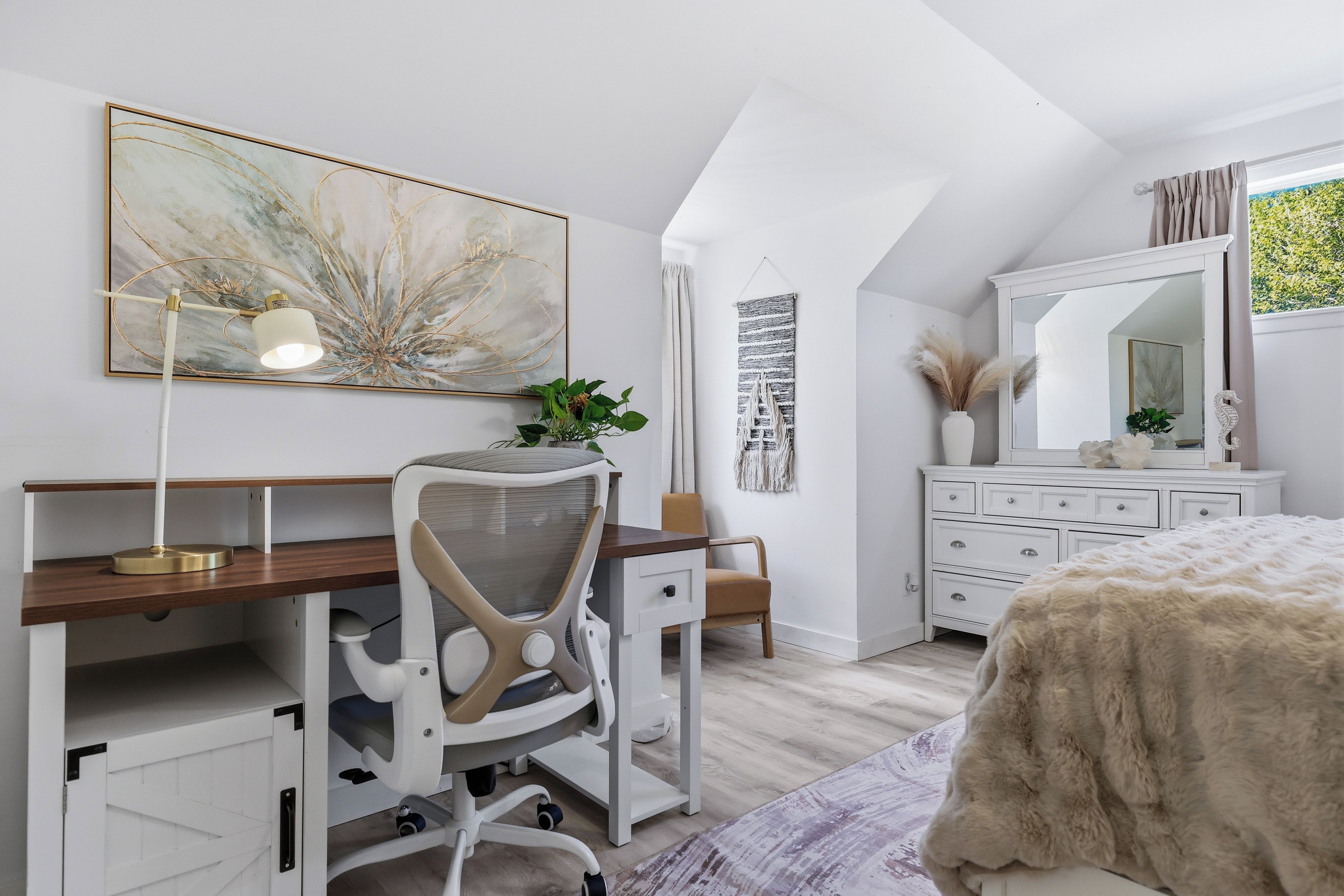 Une chambre à coucher comprenant un bureau, une chaise, un lit, une commode, un miroir et des œuvres d’art.