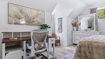 Une chambre à coucher comprenant un bureau, une chaise, un lit, une commode, un miroir et des œuvres d’art.