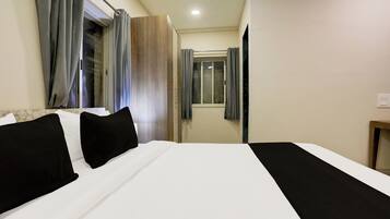 Habitación de hotel con una cama grande, una mesita de noche, una ventana con cortinas y una puerta que da a otra habitación.