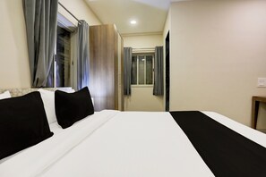 Habitación de hotel con una cama grande, una mesita de noche, una ventana con cortinas y una puerta que da a otra habitación.