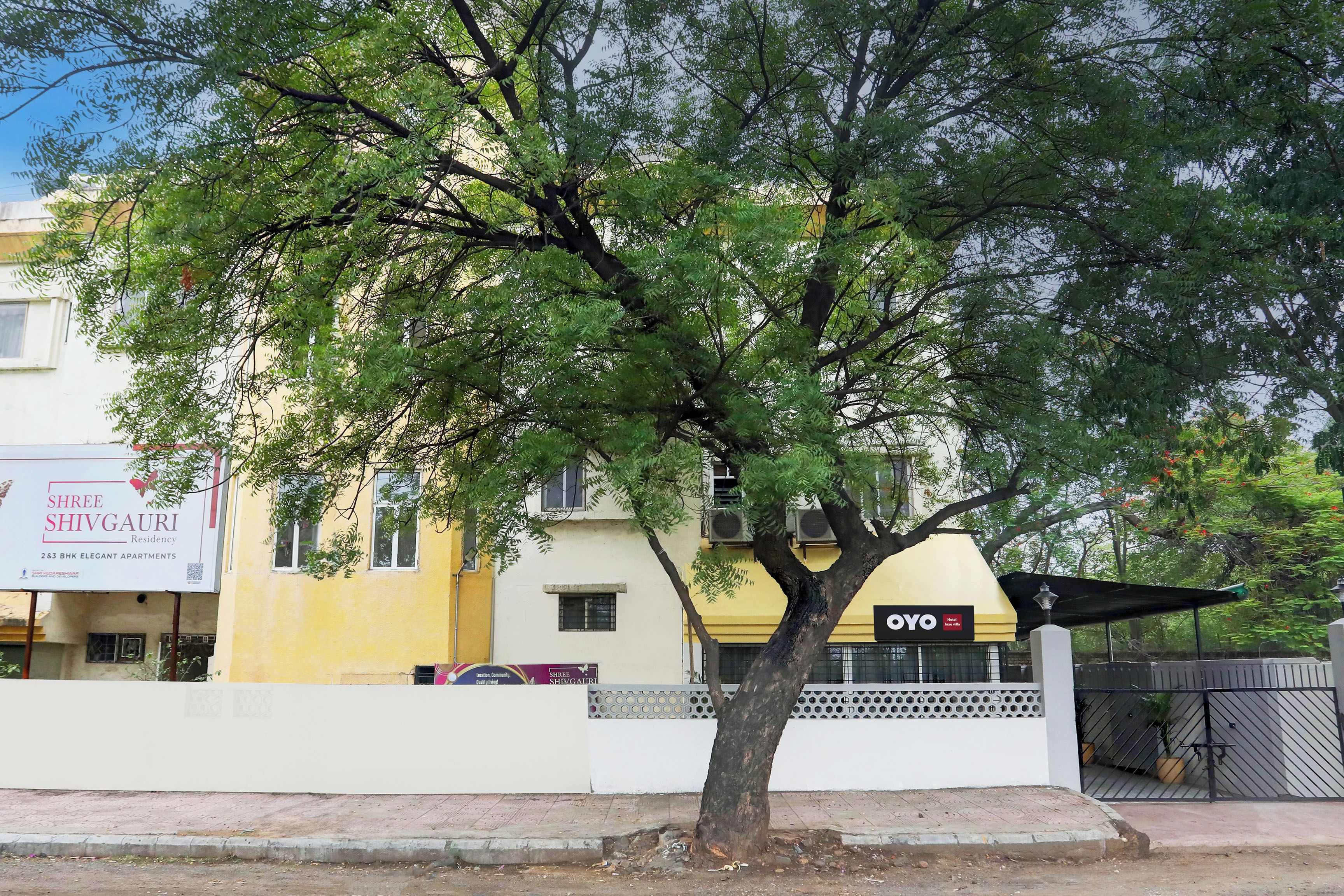 A tree-lined street with a hotel named 'OYO' and a building with a sign for 'Shree Shivgauri Residency.'