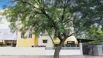 Una calle arbolada con un hotel llamado 'OYO' y un edificio con un letrero que dice 'Shree Shivgauri Residency'.